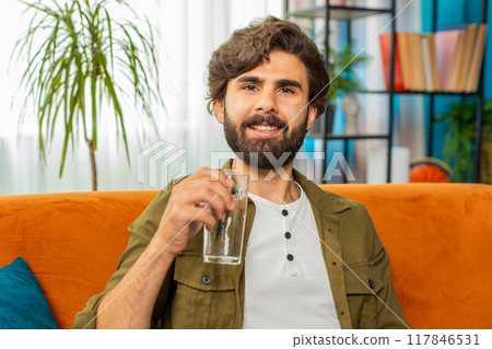 Thirsty middle eastern man at home holding glass of natural aqua make sips drinking filtered water 117846531