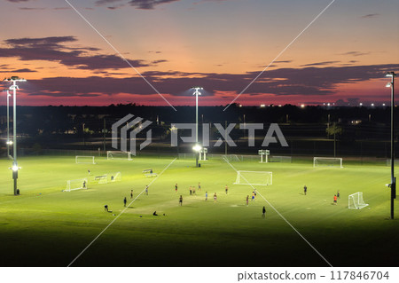 People playing soccer game on illuminated public stadium at sunset. Active way of life concept People playing soccer game on illuminated public stadium at sunset. Active way of life concept 117846704