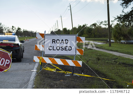 Police patrol car at yellow protective barrier at street construction site. Warning road sign about utility work 117846712