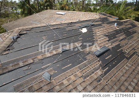 Damaged house roof with missing shingles after hurricane Ian in Florida. Consequences of natural disaster 117846831