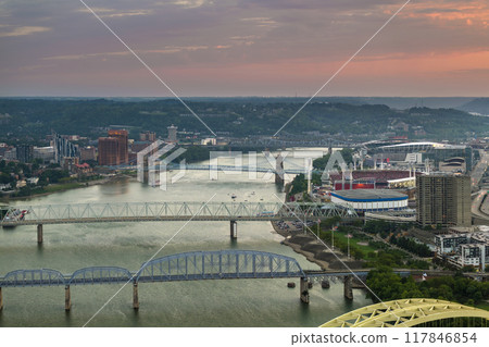 Downtown district of Cincinnati city in Ohio, USA at sunset with driving cars traffic on bridge and brightly illuminated high skyscraper buildings. American travel destination 117846854