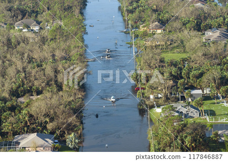 Flooded american street with moving vehicles and surrounded with water houses in Florida residential area. Consequences of hurricane natural disaster Flooded american street with moving vehicles and surrounded with water houses in Florida residential area. Consequences of hurricane natural disaster 117846887