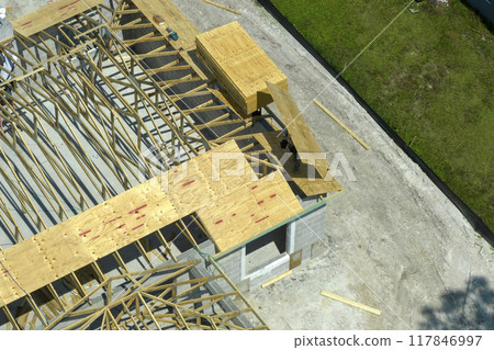Builders working on roof construction of unfinished residential house with wooden frame structure in Florida suburban area. Housing development concept 117846997
