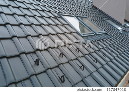 Closeup snow guard for safety in winter on house roof top covered with ceramic shingles. Tiled covering of building Closeup snow guard for safety in winter on house roof top covered with ceramic shingles. Tiled covering of building 117847018