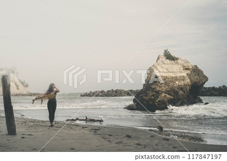 Young woman standing with surfboard in windy ocean Young woman standing with surfboard in windy ocean 117847197