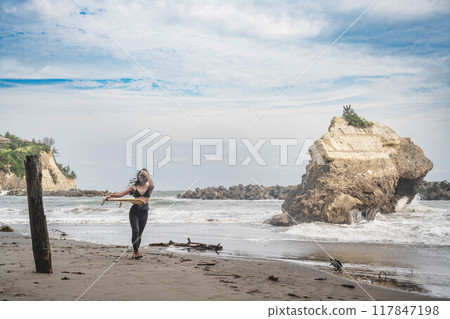 在風大的大海中拿著衝浪板站立的年輕女子 在風大的大海中拿著衝浪板站立的年輕女子 117847198