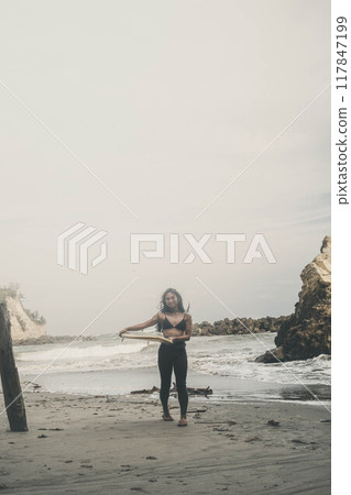 Young woman standing with surfboard in windy ocean Young woman standing with surfboard in windy ocean 117847199