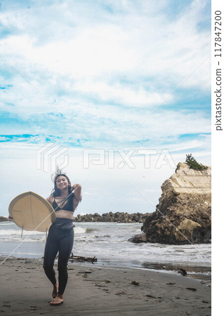 在風大的大海中拿著衝浪板站立的年輕女子 在風大的大海中拿著衝浪板站立的年輕女子 117847200