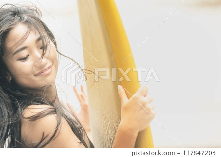 Young woman standing with surfboard in windy ocean 117847203