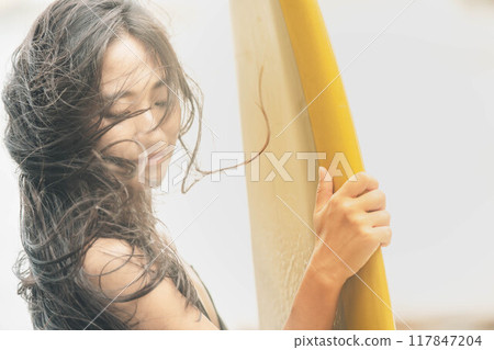 在風大的大海中拿著衝浪板站立的年輕女子 在風大的大海中拿著衝浪板站立的年輕女子 117847204