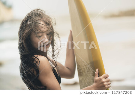 在風大的大海中拿著衝浪板站立的年輕女子 在風大的大海中拿著衝浪板站立的年輕女子 117847208