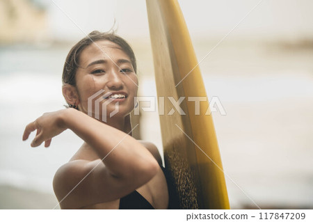Young woman standing with surfboard in windy ocean Young woman standing with surfboard in windy ocean 117847209