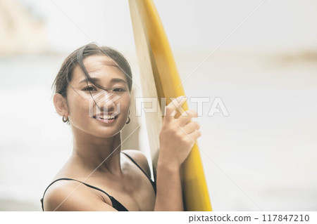 Young woman standing with surfboard in windy ocean 117847210