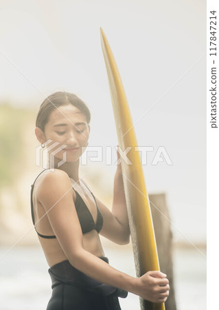 在風大的大海中拿著衝浪板站立的年輕女子 117847214