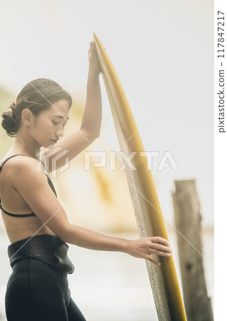 在風大的大海中拿著衝浪板站立的年輕女子 在風大的大海中拿著衝浪板站立的年輕女子 117847217