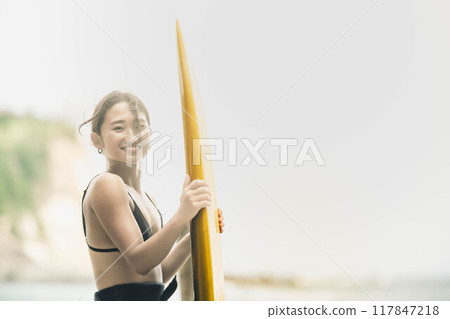 在風大的大海中拿著衝浪板站立的年輕女子 117847218