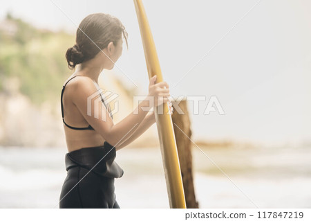 在風大的大海中拿著衝浪板站立的年輕女子 在風大的大海中拿著衝浪板站立的年輕女子 117847219