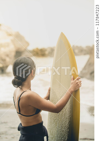 在風大的大海中拿著衝浪板站立的年輕女子 在風大的大海中拿著衝浪板站立的年輕女子 117847223