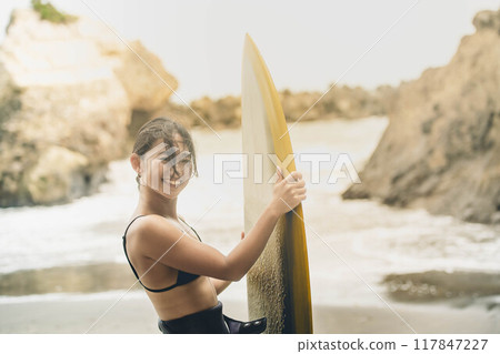 在風大的大海中拿著衝浪板站立的年輕女子 在風大的大海中拿著衝浪板站立的年輕女子 117847227