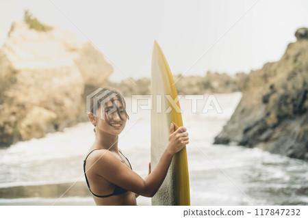 在風大的大海中拿著衝浪板站立的年輕女子 在風大的大海中拿著衝浪板站立的年輕女子 117847232