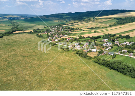 Aerial landscape view of village houses and distant green cultivated agricultural fields with growing crops on bright summer day Aerial landscape view of village houses and distant green cultivated agricultural fields with growing crops on bright summer day 117847391