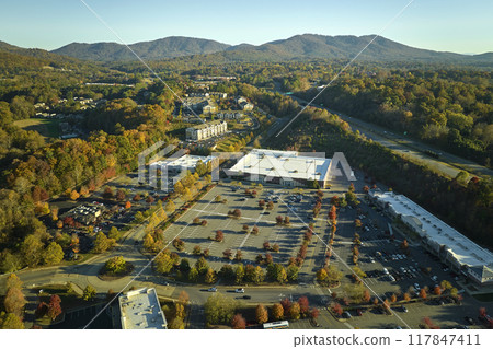 Aerial view grocery shopping mall and many colorful cars parked on parking lot with lines and markings for parking places and directions. Place for vehicles in front of a strip mall plaza Aerial view grocery shopping mall and many colorful cars parked on parking lot with lines and markings for parking places and directions. Place for vehicles in front of a strip mall plaza 117847411