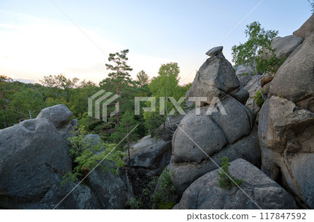 Huge rocky boulder formations high in mountains with growing trees on summer sunny day Huge rocky boulder formations high in mountains with growing trees on summer sunny day 117847592