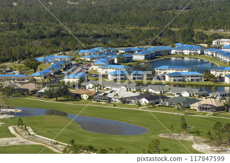 Hurricane damaged apartment buildings rooftops covered with protective plastic tarp against rain water leaking until replacement of asphalt shingles. Aftermath of natural disaster 117847599