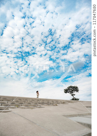 A young woman walking next to a tree on the beach under a blue sky A young woman walking next to a tree on the beach under a blue sky 117847680
