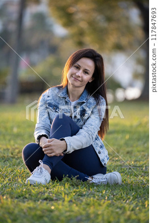 Woman sitting on grass in city park on summer day 117847693