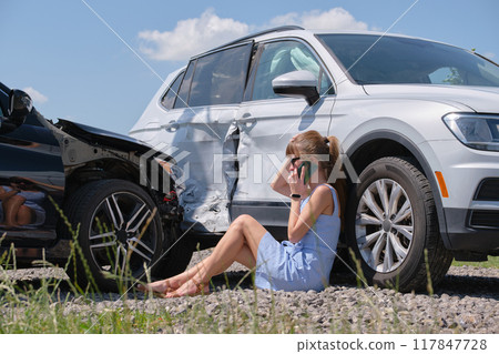 Stressed driver talking on cellphone on roadside near her smashed vehicle calling for emergency service help after car accident. Road safety and insurance concept 117847728
