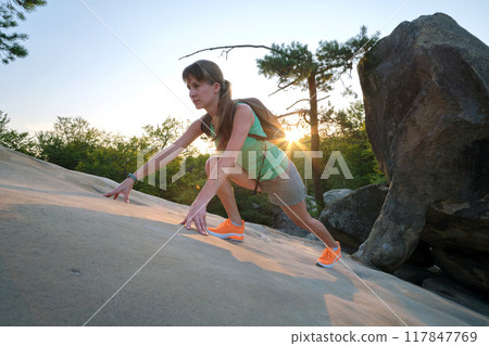 Hiker woman clambering on rocky mountain footpath in evening nature. Lonely female traveler traversing hard wilderness trail. Healthy lifestyle and sport concept 117847769