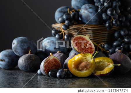 Blue grapes, blue plums, and figs on a black stone table. 117847774
