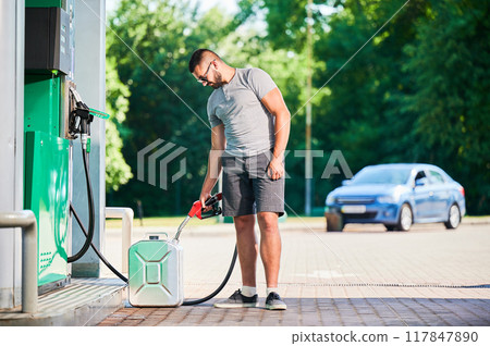 Driver refueling canister with gasoline at modern gas station. Man filling cistern with fuel in case of unforeseen circumstances. Man in casual clothes with pump nozzle on background of his car. Driver refueling canister with gasoline at modern gas station. Man filling cistern with fuel in case of unforeseen circumstances. Man in casual clothes with pump nozzle on background of his car. 117847890