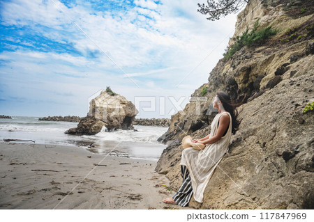 Young woman leaning against a cliff by the sea Young woman leaning against a cliff by the sea 117847969