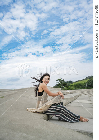 A woman sits on the beach in a strong wind 117848089