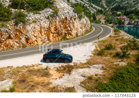 Car with a roof box stands on the side of a cliff and beautiful rocks in the background 117848128