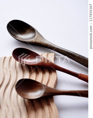 Everyday cutlery on a wooden coaster on a white background 117850167
