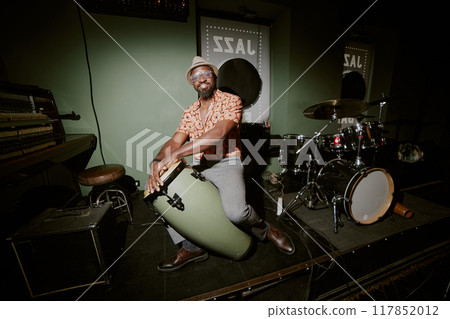 Flash photo of African American musician posing for camera with conga on stage in local bar Flash photo of African American musician posing for camera with conga on stage in local bar 117852012