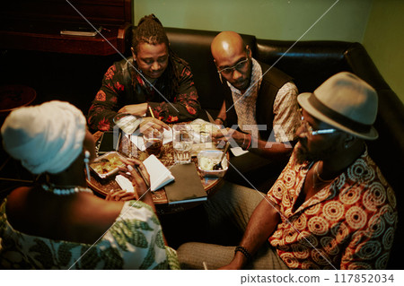 High angle view of four African American jazz musicians sitting at table in local bar having meal and discussing new album High angle view of four African American jazz musicians sitting at table in local bar having meal and discussing new album 117852034
