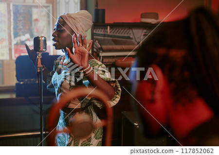 Selective focus shot of young Black woman singing jazz song in microphone during rehearsal with band 117852062
