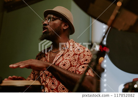 Confident African American man enjoying singing song while playing conga on stage in bar 117852082