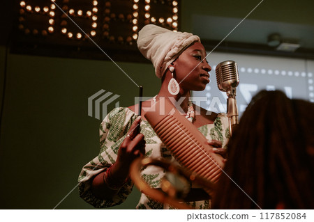 Medium low angle view shot of young African American woman singing jazz song and playing guiro 117852084