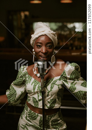 Self-confident young Black woman singing jazz song on stage in bar and looking at camera, vertical medium shot Self-confident young Black woman singing jazz song on stage in bar and looking at camera, vertical medium shot 117852099