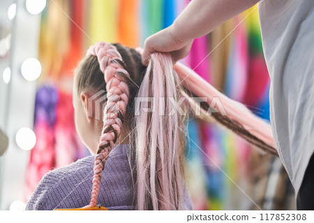 A rear view of the hands of the master who weave the kanekalon material into the hair. The master braids the child's pigtails from a pink kanekalon. With space to copy. High quality photo A rear view of the hands of the master who weave the kanekalon material into the hair. The master braids the child's pigtails from a pink kanekalon. With space to copy. High quality photo 117852308