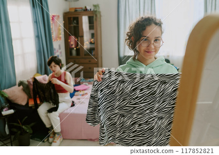 Girl holding zebra-print fabric with another person sewing and a shelf of neatly organized items in background creating a cozy and creative atmosphere Girl holding zebra-print fabric with another person sewing and a shelf of neatly organized items in background creating a cozy and creative atmosphere 117852821