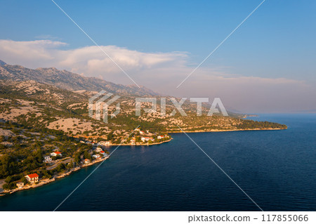 Aerial view of a picturesque coastline with mountains and serene waters on a sunny day.  117855066