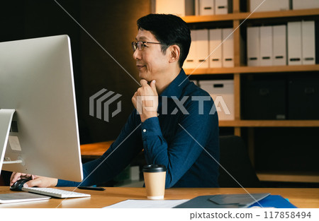 Middle-aged man facing a computer Middle-aged man facing a computer 117858494