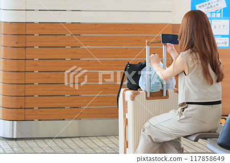 A woman waiting for a train on a bench at a station A woman waiting for a train on a bench at a station 117858649