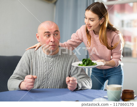 Portrait of a disgruntled man, to whom a young woman brought a plate of spinach 117860170